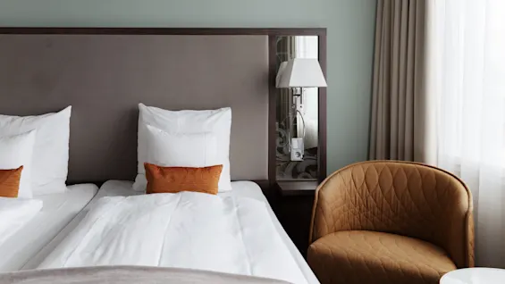 Ett mysigt hotellrum med två prydligt bäddade sängar, en inbjudande fåtölj och mjuk belysning, perfekt för avkoppling.