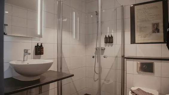 A modern bathroom featuring a white sink, a glass shower, and a toilet. A mirror with lights hangs above the sink.
