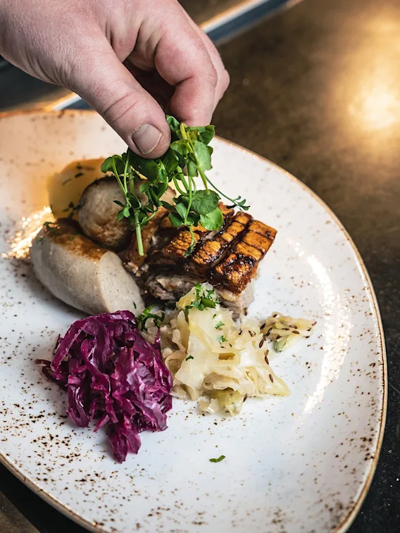 Händer som garnerar en tallrik med traditionell julmat bestående av ribbe, korv och kål.