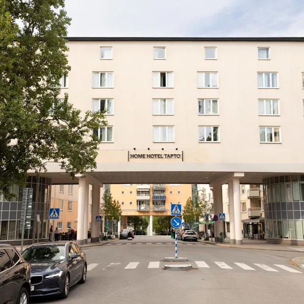 Exteriör vy av Home Hotel Tapto i Stockholm, en stor byggnad som sträcker sig över en gata med bilar och träd.