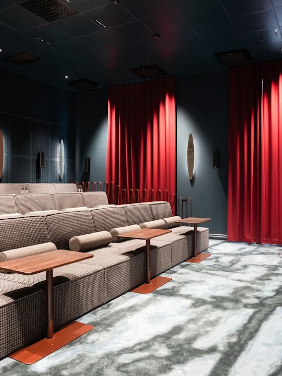 En mysig privat biograf med gradängsittplatser, individuella bord och en stor skärm, redo för en filmupplevelse.