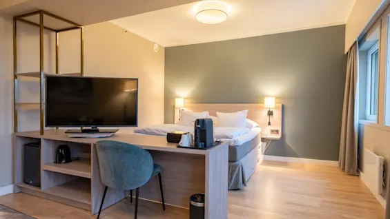 Et koselig hotellrom med en seng, et skrivebordsområde og en kaffemaskin, klart for et komfortabelt opphold.