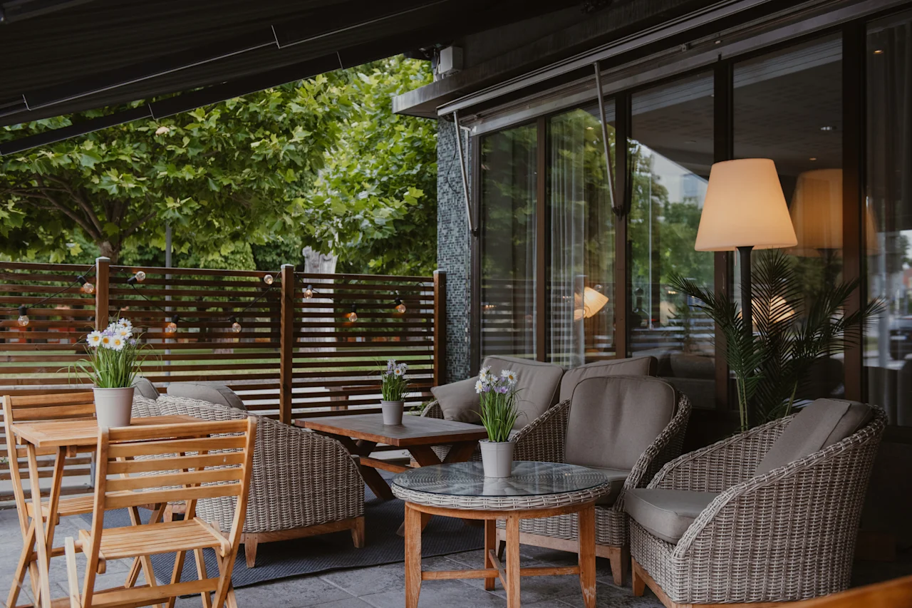 A cozy outdoor patio with comfortable seating and tables, surrounded by greenery, perfect for relaxation.