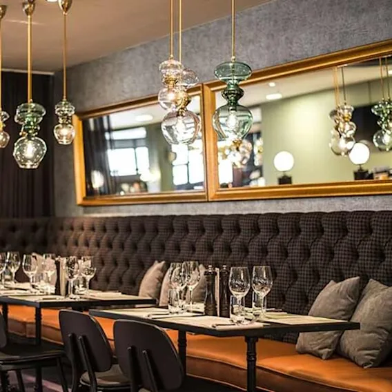 Elegant restaurant Brasserie Absint at Clarion Hotel Winn with dark tufted seating, set tables, and hanging glass lamps.