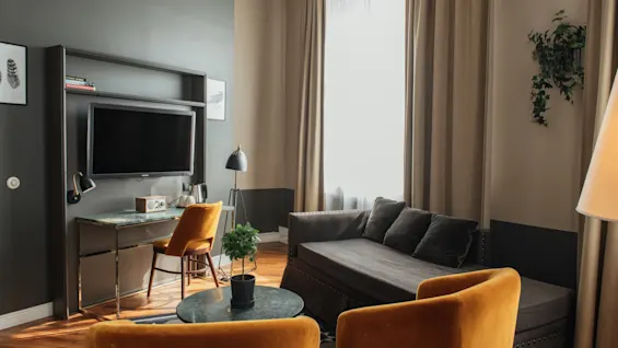Et stilfuldt hotelværelse med et komfortabelt siddeområde med sofa og lænestole, samt et funktionelt skrivebord og TV.