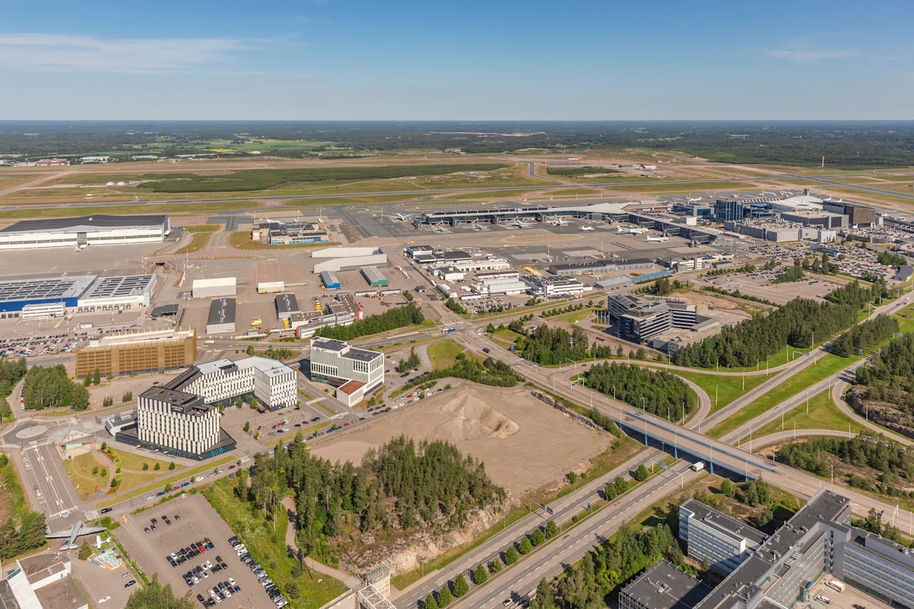 Et luftfoto, der viser en travl lufthavn, nærliggende kommercielle bygninger, indviklede vejnet og frodige grønne landskaber.
