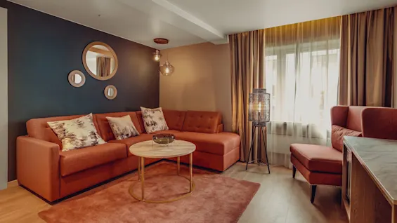 A cozy living room with a terracotta sectional sofa, round coffee table, and decorative mirrors on a dark accent wall.