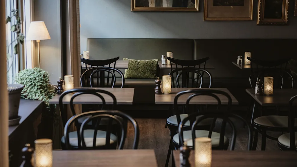 Mysig restauranginredning med mörka träbord, svarta stolar, en grön bänk och varmt levande ljus.