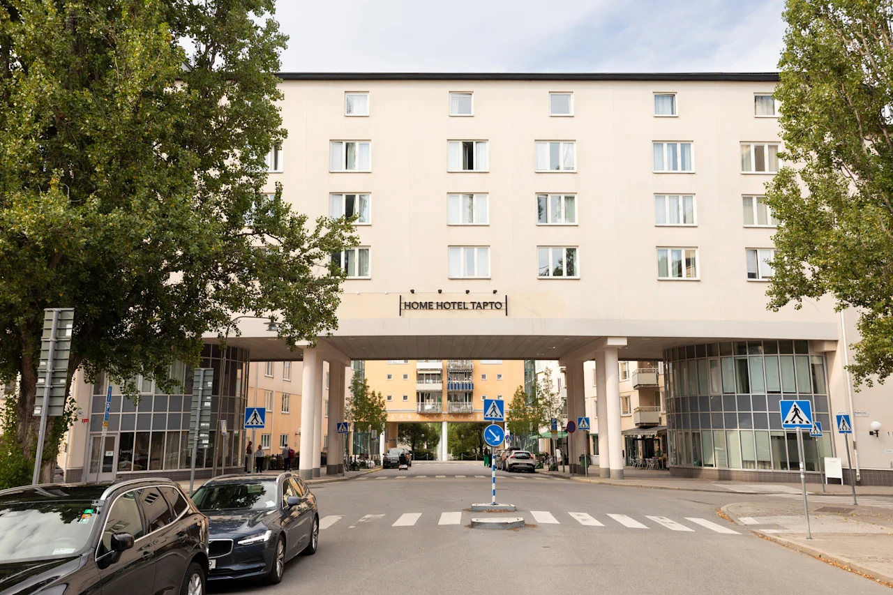 Exteriör vy av Home Hotel Tapto i Stockholm, en stor byggnad som sträcker sig över en gata med bilar och träd.