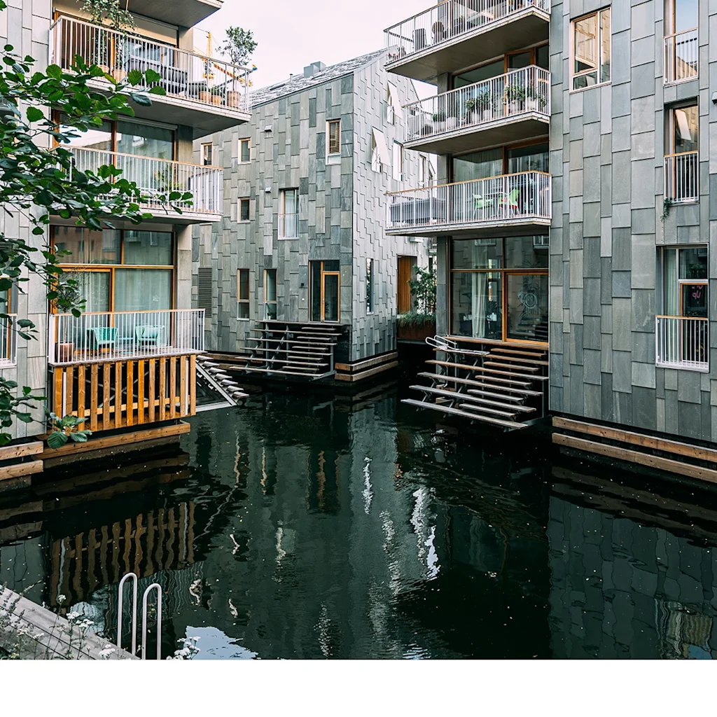 Moderne bygninger med balkonger som vender ut mot en rolig kanal, med unike flislagte fasader og trapper som fører ned til vannet.