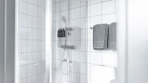 Puhdas, moderni kylpyhuone suihkulla, hygieniatuotteilla ja puhtailla pyyhkeillä, käyttövalmiina.