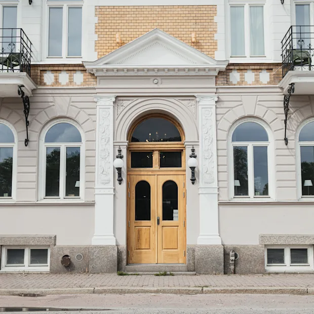 Kaksiosainen puuovi sijaitsee klassisen julkisivun keskellä, jossa on kaarevat ikkunat ja koristeelliset pylväät. Tiili- ja stukkirakennuksessa on pienet parvekkeet ja kiviaskeleet johtavat sisäänkäynnille.