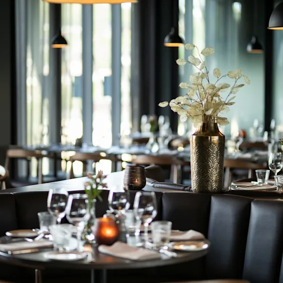 Et stilig restaurantinteriør med dekkede bord, komfortable sitteplasser og varm belysning, som skaper en innbydende atmosfære.