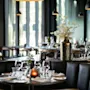 Et stilig restaurantinteriør med dekkede bord, komfortable sitteplasser og varm belysning, som skaper en innbydende atmosfære.
