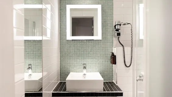 A stylish bathroom at Home Hotel Grand Bodø featuring a square sink, illuminated mirror, and green tiled accent wall.