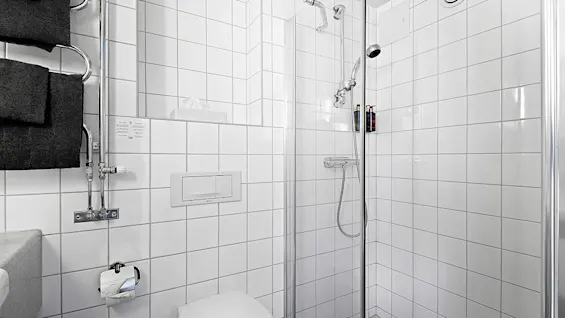 A white tiled bathroom with a shower, towel, and toilet in a clean, bright setting.