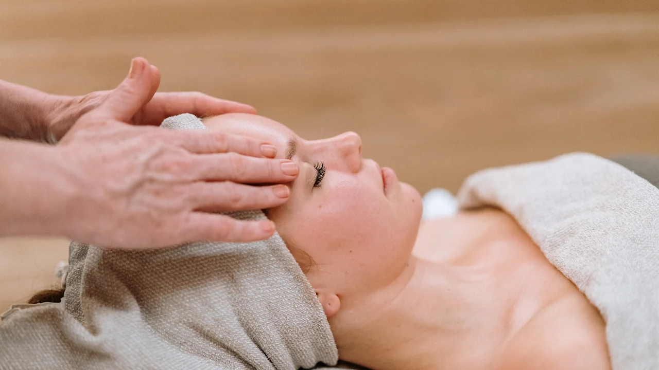 Person modtager ansigtsmassage, ligger på en spa-seng, dækket med håndklæder, i et roligt rum med trægulv.