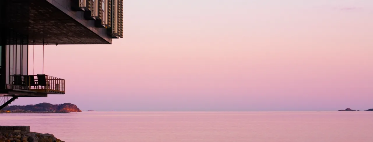 En moderne bygning overhænger stille havvand i skumringen, med en pastellignende himmel.