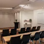 Valoisa ja moderni kokoushuone, jossa on pöytiä, tuoleja, projektori, valkotaulu ja fläppitaulu, valmiina tuottavaan istuntoon.
