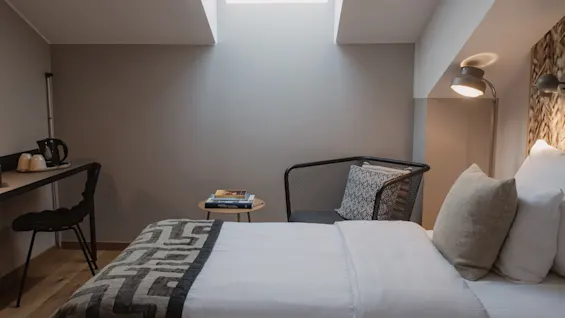 Viihtyisä hotellihuone, jossa sänky, työpöytä, tuoli ja kattoikkuna, moderni sisustus ja luonnonvaloa.