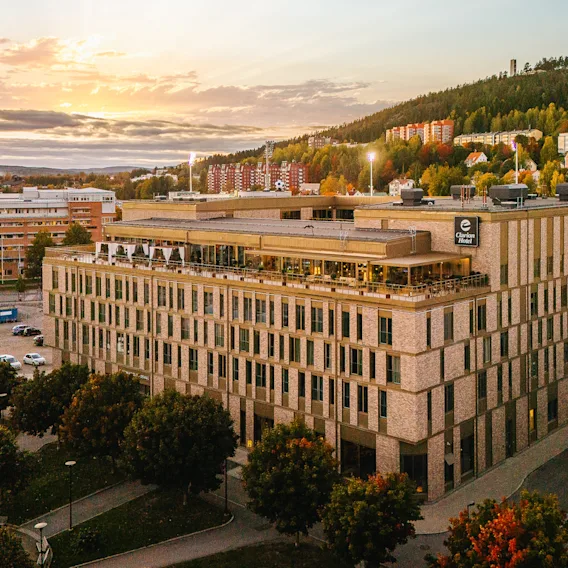 En imponerande hotellbyggnad med en livlig takterrass, badad i solnedgångens varma sken, med en naturskön sluttning bakom.