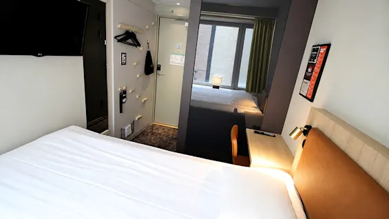 Moderni ja valoisa hotellihuone, jossa on mukava sänky, työpöytä ja suuri ikkunaa heijastava peili.