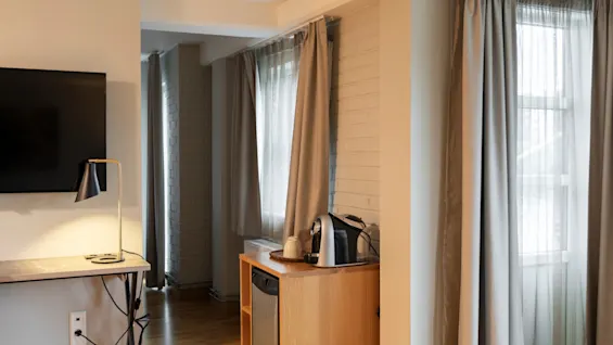 Et koselig hotellrom med TV, kaffestasjon og lyse vinduer med gardiner, som tilbyr et komfortabelt opphold.