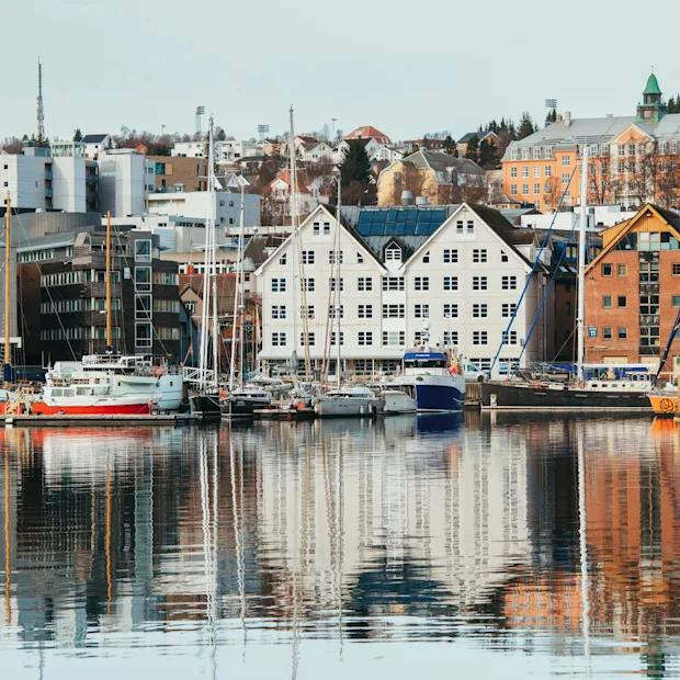 A scenic waterfront view of a city with buildings and boats reflected in the calm water.