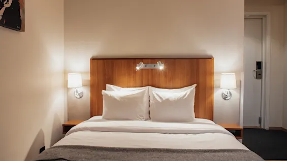 A cozy hotel room with a neatly made bed, white linens, and a wooden headboard. Home Hotel Kung Oscar.