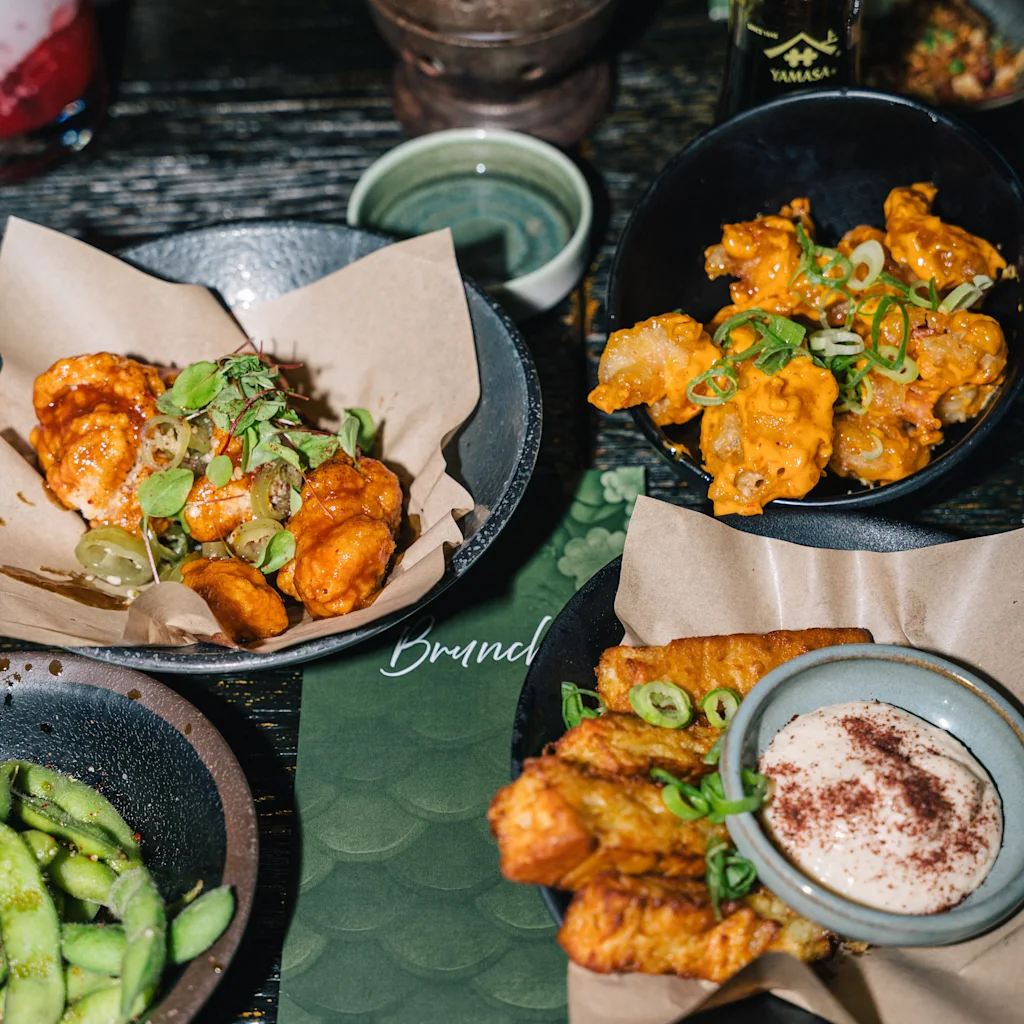 Ett bord fyllt med olika läckra rätter, inklusive friterade bitar med såser, edamame och en meny som säger Brand ETOTOSO.