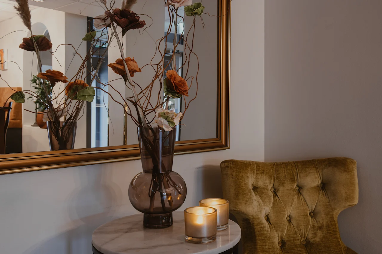 A cozy corner at Home Hotel Kung Oscar with a decorative vase, lit candles on a marble table, and a plush armchair.