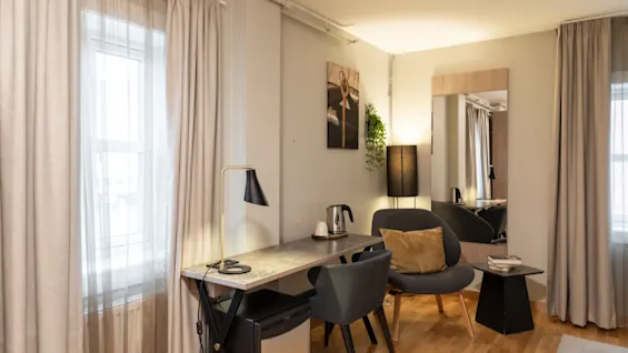 Et koselig hotellrom med skrivebord, to stoler og en lenestol, perfekt for arbeid eller avslapning, badet i naturlig lys.