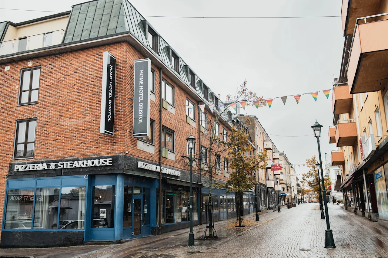 Katunäkymä tiilirakennuksella, jossa on hotelli ja ravintola. Värikkäät viirit roikkuvat märän mukulakivikadun yllä.