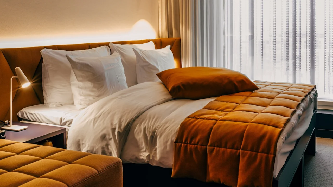 Viihtyisä ja moderni hotellihuone, jossa on mukava sänky, lämmin valaistus ja suuri ikkuna ohuilla verhoilla.