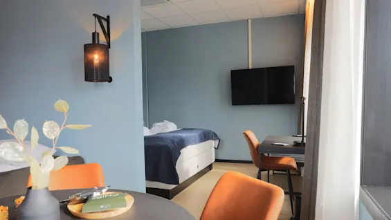 A modern hotel room with a bed, desk, chair, wall-mounted TV, and decorative lighting, creating a cozy atmosphere.