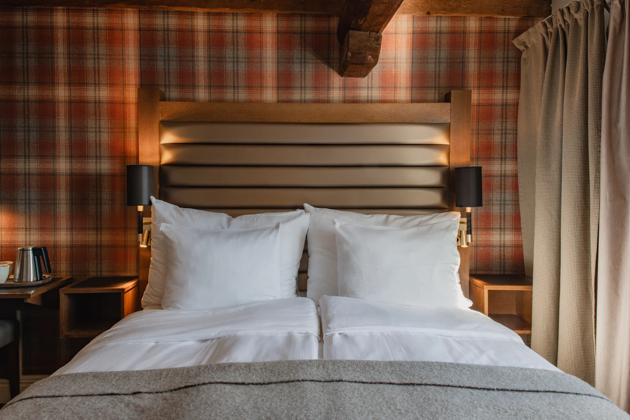 Et hyggeligt hotelværelse med en stor seng, ternet tapet og varm belysning, der indbyder til et behageligt ophold.