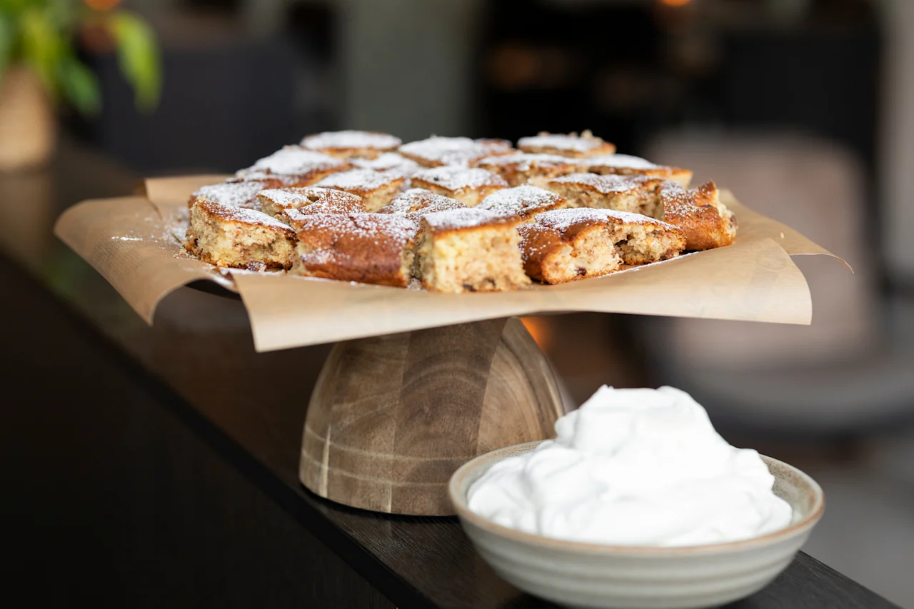 Herkullinen neliönmuotoinen kakku tomusokerilla, tarjoillaan kermavaahdon kera, valmiina nautittavaksi.