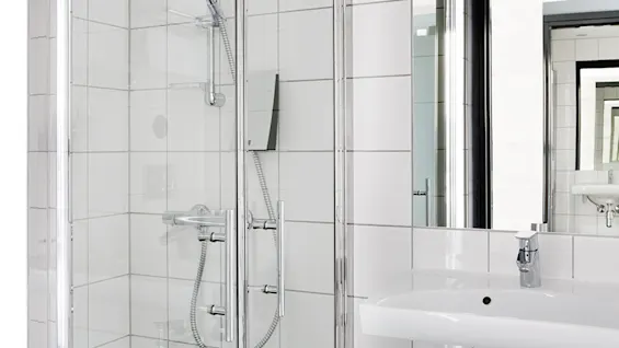 A modern bathroom corner with a glass shower enclosure and a white sink with a mirror.
