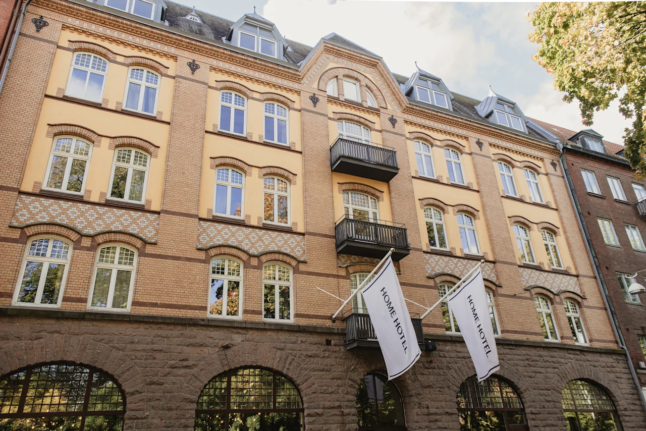 Home Hotel Norre Park i Halmstad, en fleretagers bygning med murstens- og gul facade, og flag der viser HOME HOTEL.
