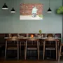 Et koselig restaurantinteriør med et langt spisebord dekket med glass og bestikk, en brun skinnbenk og trestoler. Et bilde av en scooter henger på veggen.
