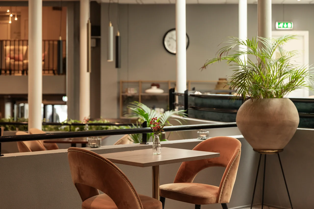 A cozy hotel lounge area with comfortable seating, lush green plants, and a warm ambiance at Home Hotel Grand Bodø.
