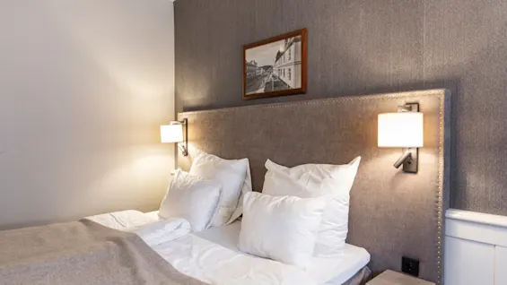 A comfortable and inviting hotel room at Home Hotel Grand Bodø, featuring a neatly made bed with white linens and soft lighting.