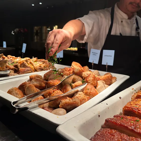 Kokk strør ferske urter over medisterkaker og juleribbe på en staselig julebuffet på hotellet.