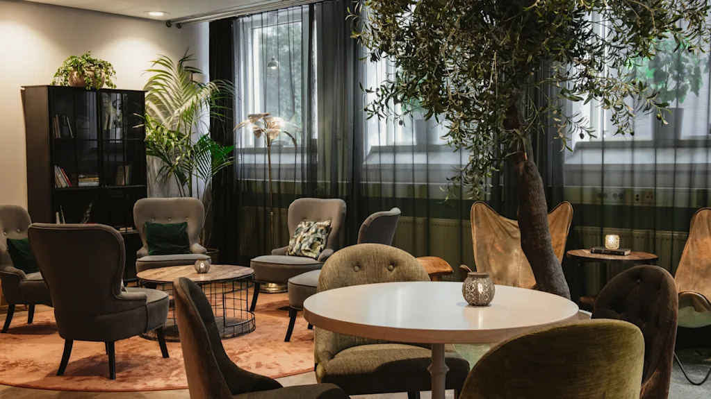 A comfortable and inviting lounge area at Home Hotel Uppsala with various seating, tables, and lush green plants.