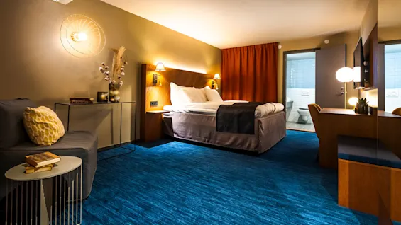 Ett modernt hotellrum med en väl bäddad säng, varmt ljus och en öppen badrumsdörr i en välutrustad miljö.