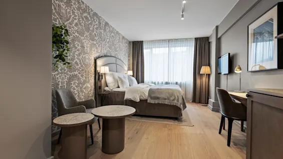 A stylish hotel room featuring a comfortable bed, a cozy seating area, and a functional workspace.