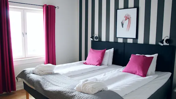 Bright hotel room featuring a double bed with pink pillows, matching curtains, and a striped accent wall with flamingo art.