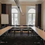 Tilava kokoushuone U-muotoisella pöytäjärjestelyllä, mustilla tuoleilla, suurilla ikkunoilla ja valkotaululla, valmiina konferenssiin.