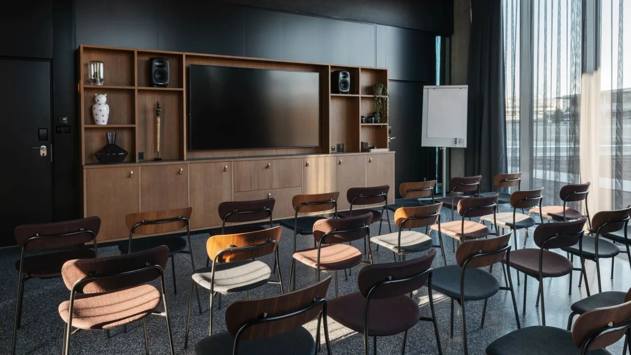 Rows of empty chairs facing a wooden cabinet with a large screen, suggesting a modern meeting or lecture room.