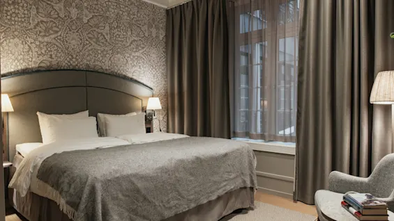 Ett mysigt hotellrum med en stor säng, mjuka sängkläder, varm belysning och en bekväm fåtölj vid fönstret.